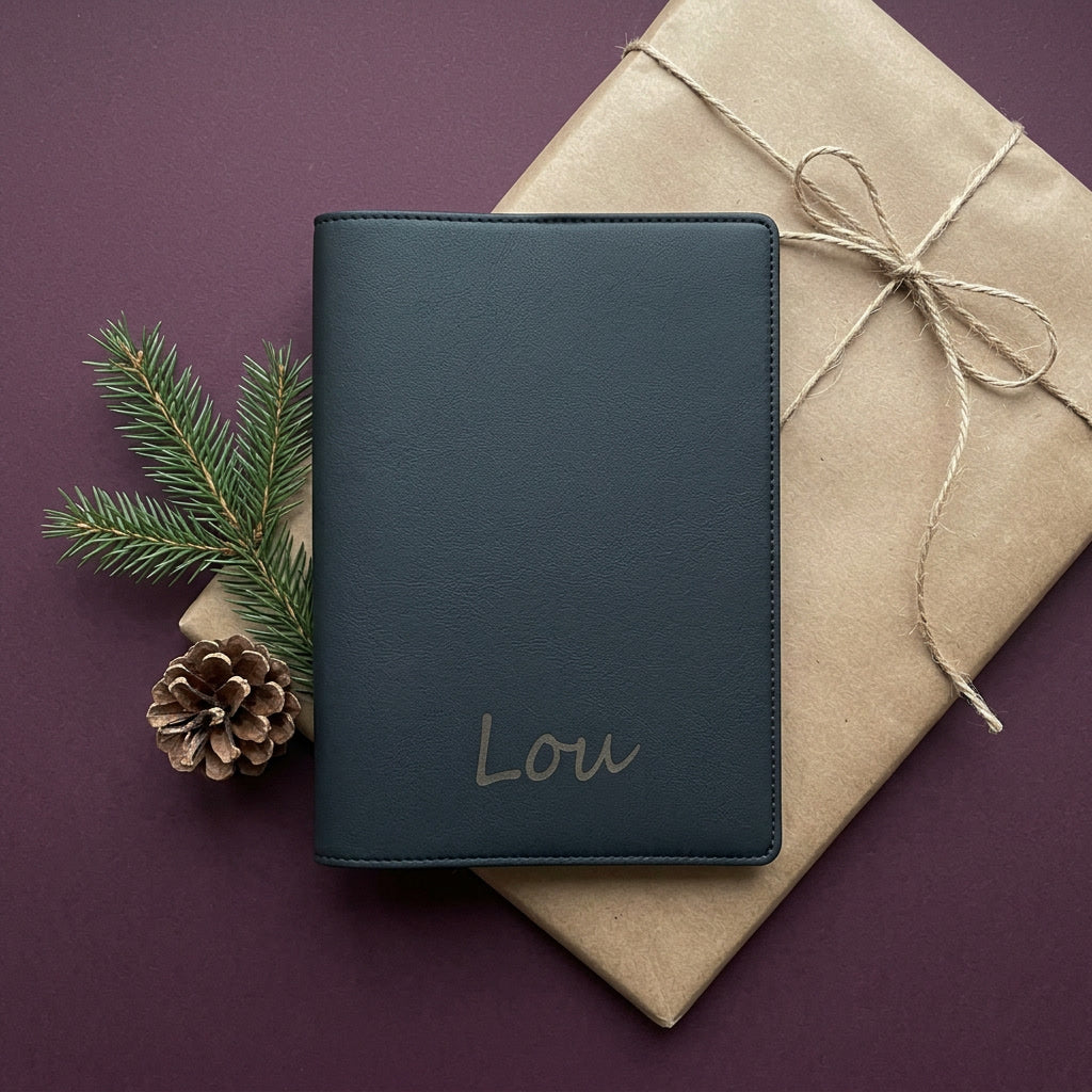 Mise en scène : protège carnet de santé gravé « Lou » dans un papier kraft, branche de sapin
