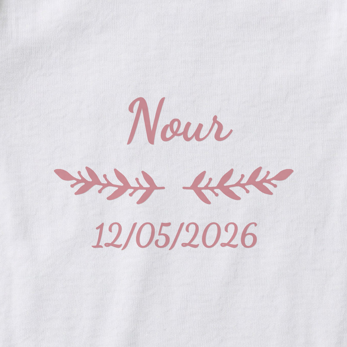 Body bébé personnalisé Nour — gros plan du marquage « Nour », ornement Rameaux et date de naissance « 12/05/2026 »