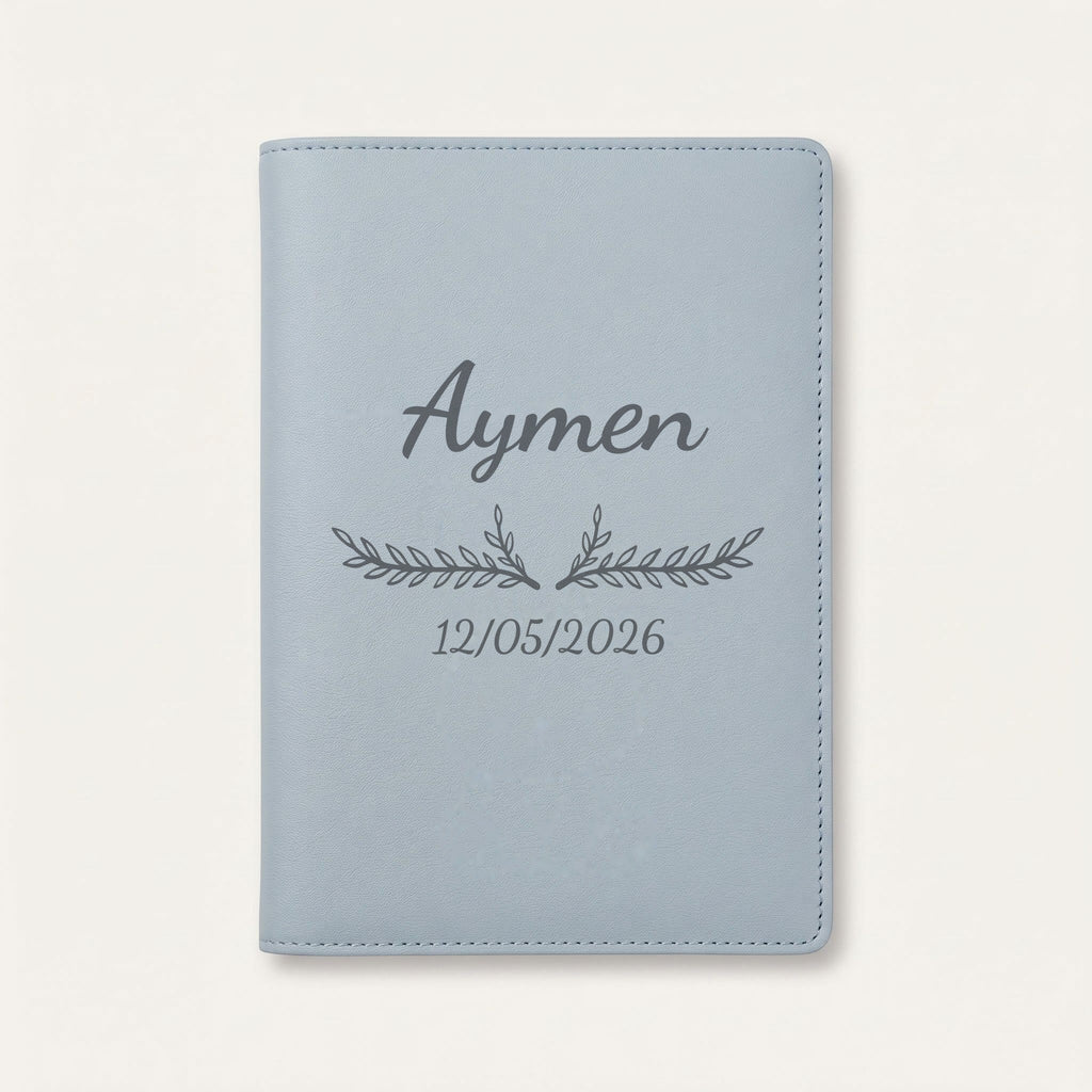 Protège carnet de santé personnalisé Aymen — Bleu nuage — prénom « Aymen », ornement Bouquet et date de naissance « 12/05/2026 » gravés