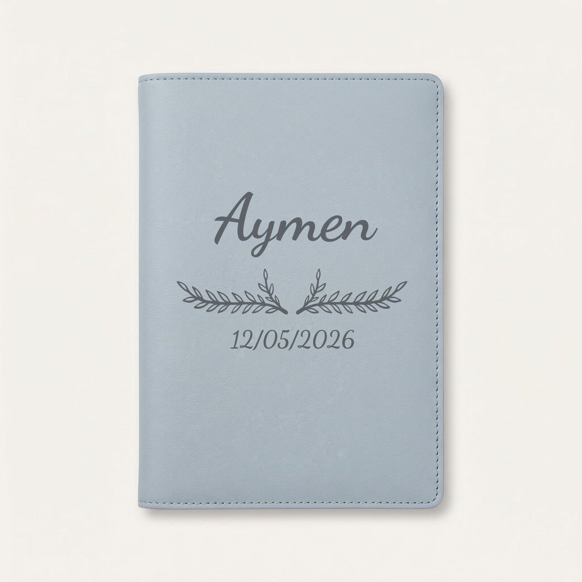 Protège carnet de santé personnalisé Aymen — Bleu nuage — prénom « Aymen », ornement Bouquet et date de naissance « 12/05/2026 » gravés
