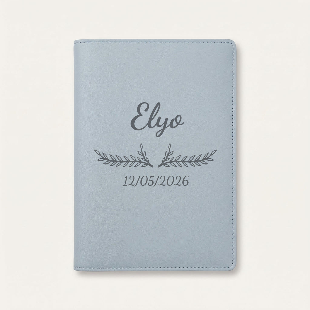 Protège carnet de santé personnalisé Elyo — Bleu nuage — prénom « Elyo », ornement Bouquet et date de naissance « 12/05/2026 » gravés