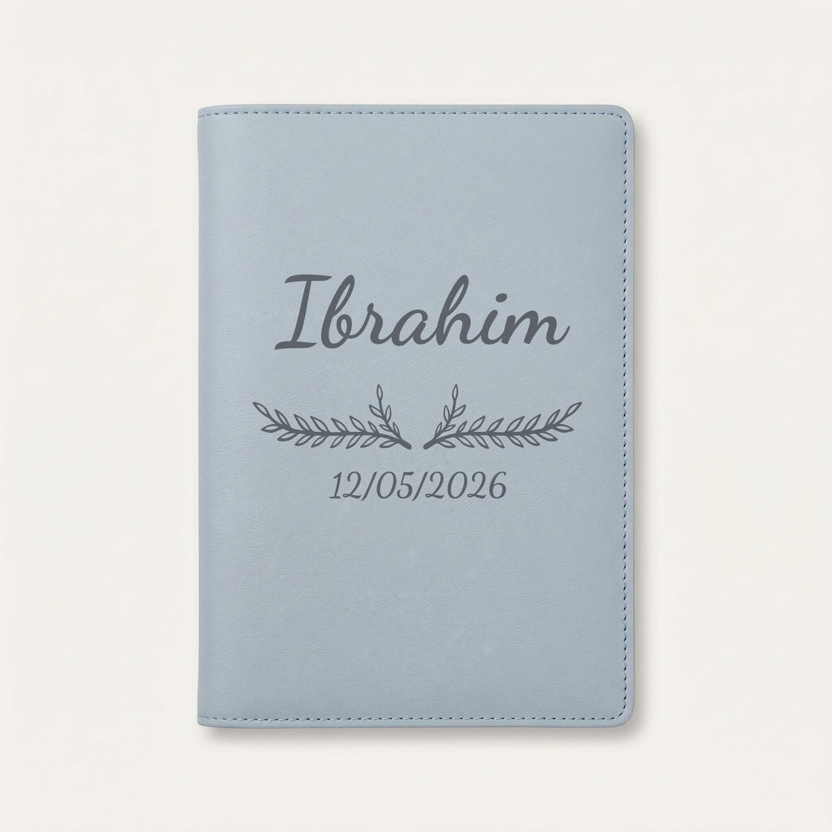 Protège carnet de santé personnalisé Ibrahim — Bleu nuage — prénom « Ibrahim », ornement Bouquet et date de naissance « 12/05/2026 » gravés