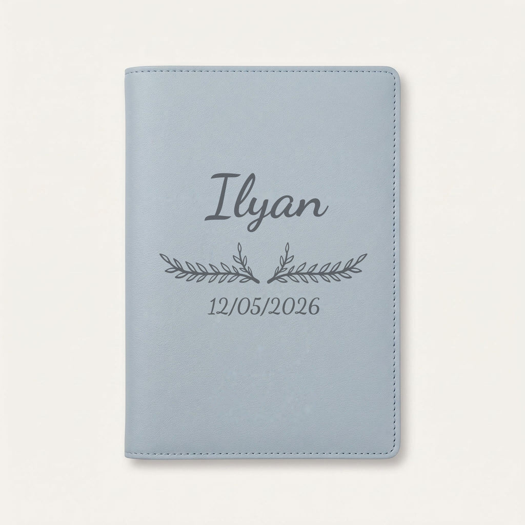Protège carnet de santé personnalisé Ilyan — Bleu nuage — prénom « Ilyan », ornement Bouquet et date de naissance « 12/05/2026 » gravés
