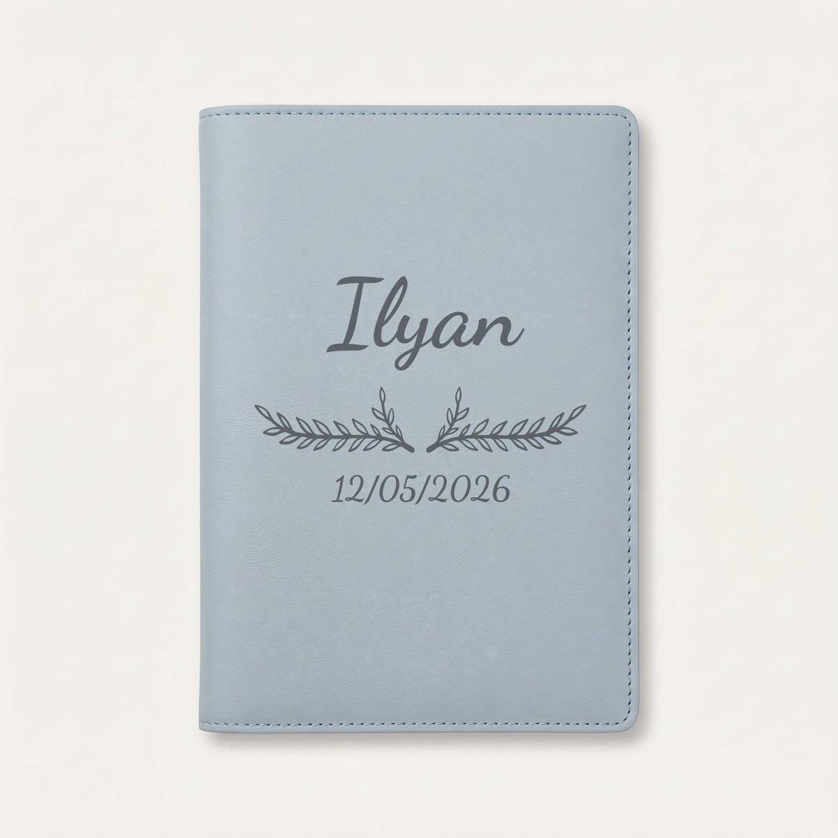 Protège carnet de santé personnalisé Ilyan — Bleu nuage — prénom « Ilyan », ornement Bouquet et date de naissance « 12/05/2026 » gravés