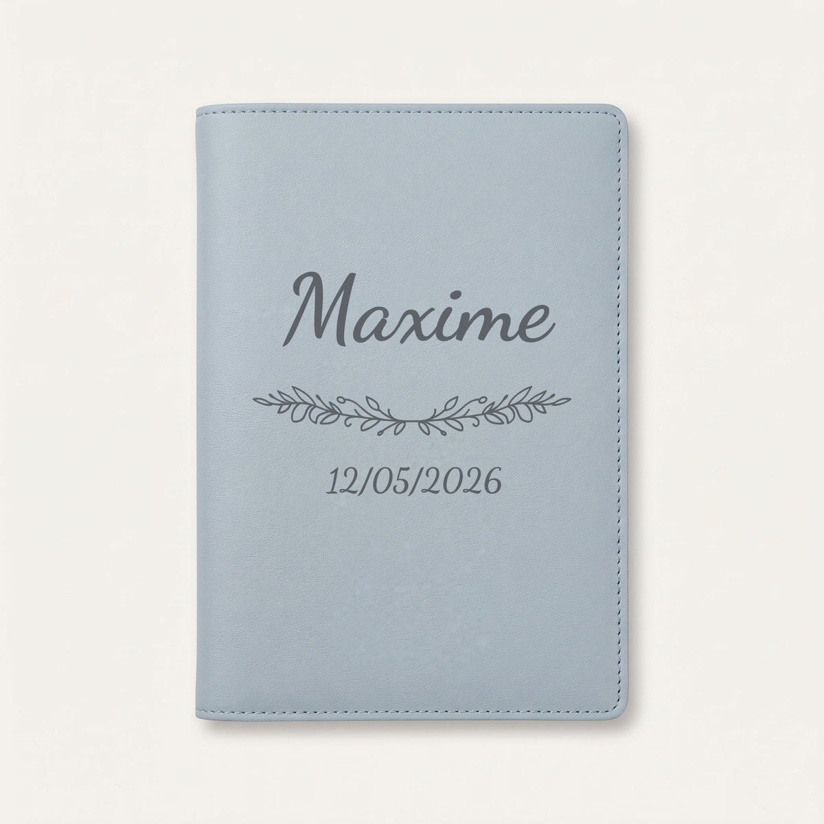 Protège carnet de santé personnalisé Maxime — Bleu nuage — prénom « Maxime », ornement Guirlande et date de naissance « 12/05/2026 » gravés