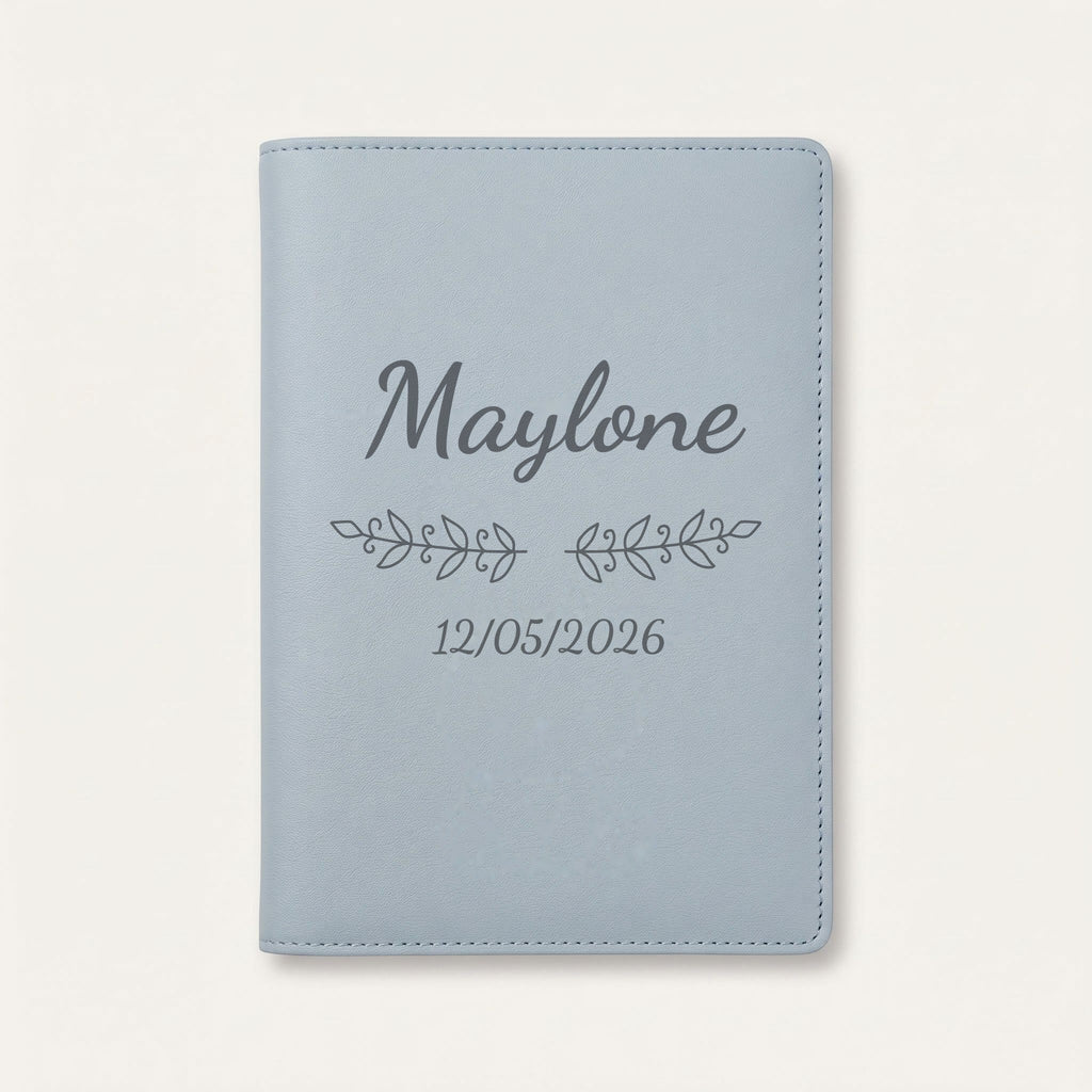 Protège carnet de santé personnalisé Maylone — Bleu nuage — prénom « Maylone », ornement Volutes et date de naissance « 12/05/2026 » gravés