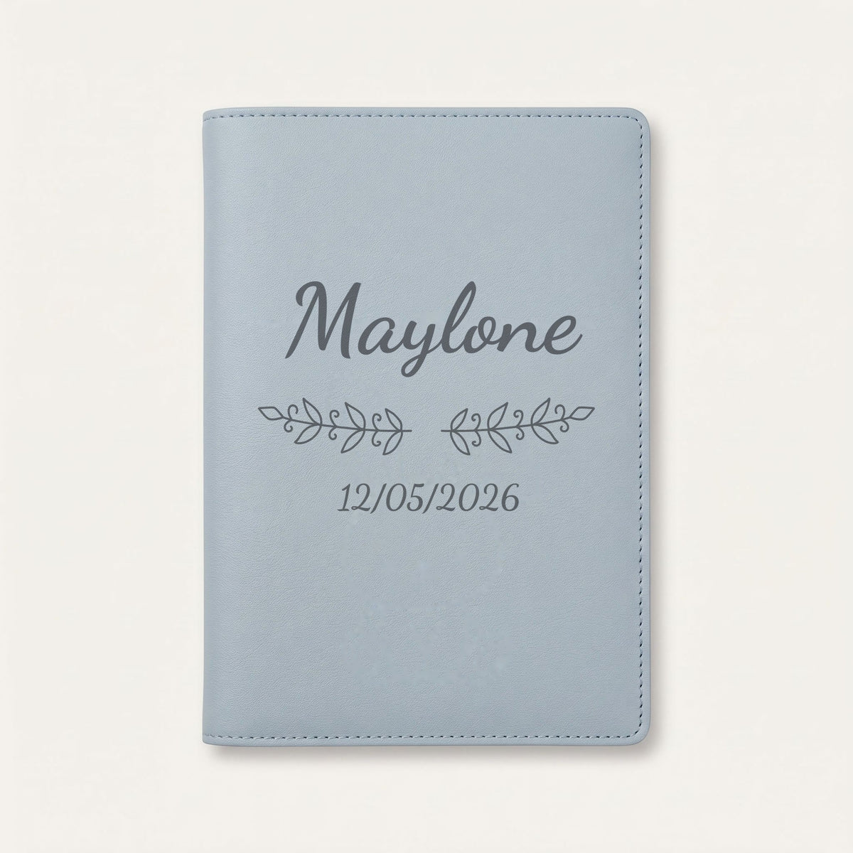 Protège carnet de santé personnalisé Maylone — Bleu nuage — prénom « Maylone », ornement Volutes et date de naissance « 12/05/2026 » gravés