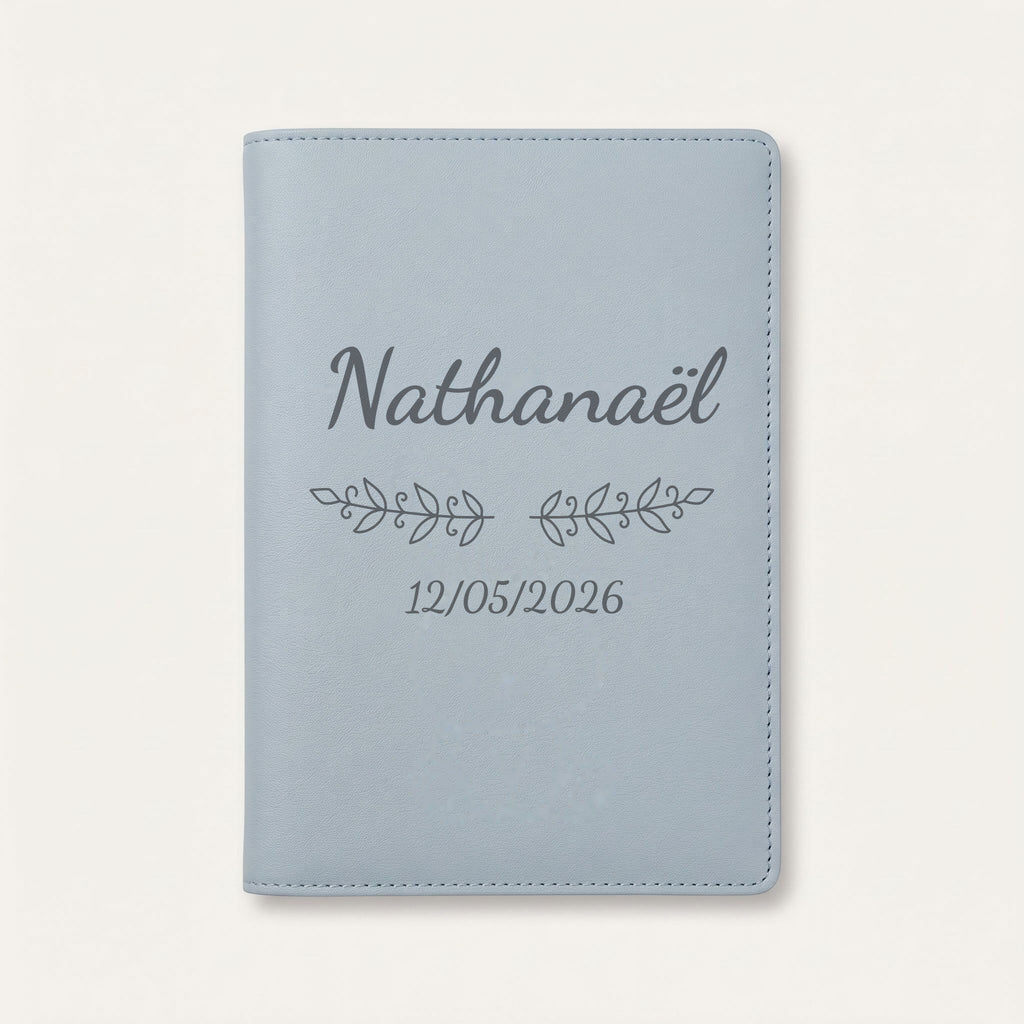Protège carnet de santé personnalisé Nathanaël — Bleu nuage — prénom « Nathanaël », ornement Volutes et date de naissance « 12/05/2026 » gravés