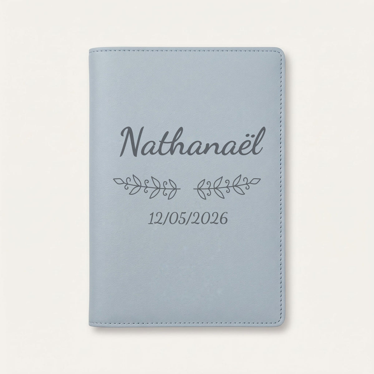Protège carnet de santé personnalisé Nathanaël — Bleu nuage — prénom « Nathanaël », ornement Volutes et date de naissance « 12/05/2026 » gravés