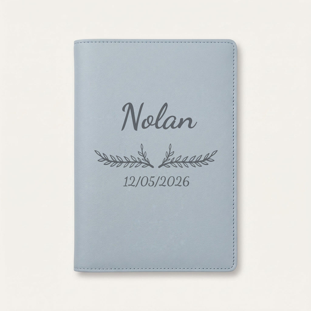 Protège carnet de santé personnalisé Nolan — Bleu nuage — prénom « Nolan », ornement Bouquet et date de naissance « 12/05/2026 » gravés