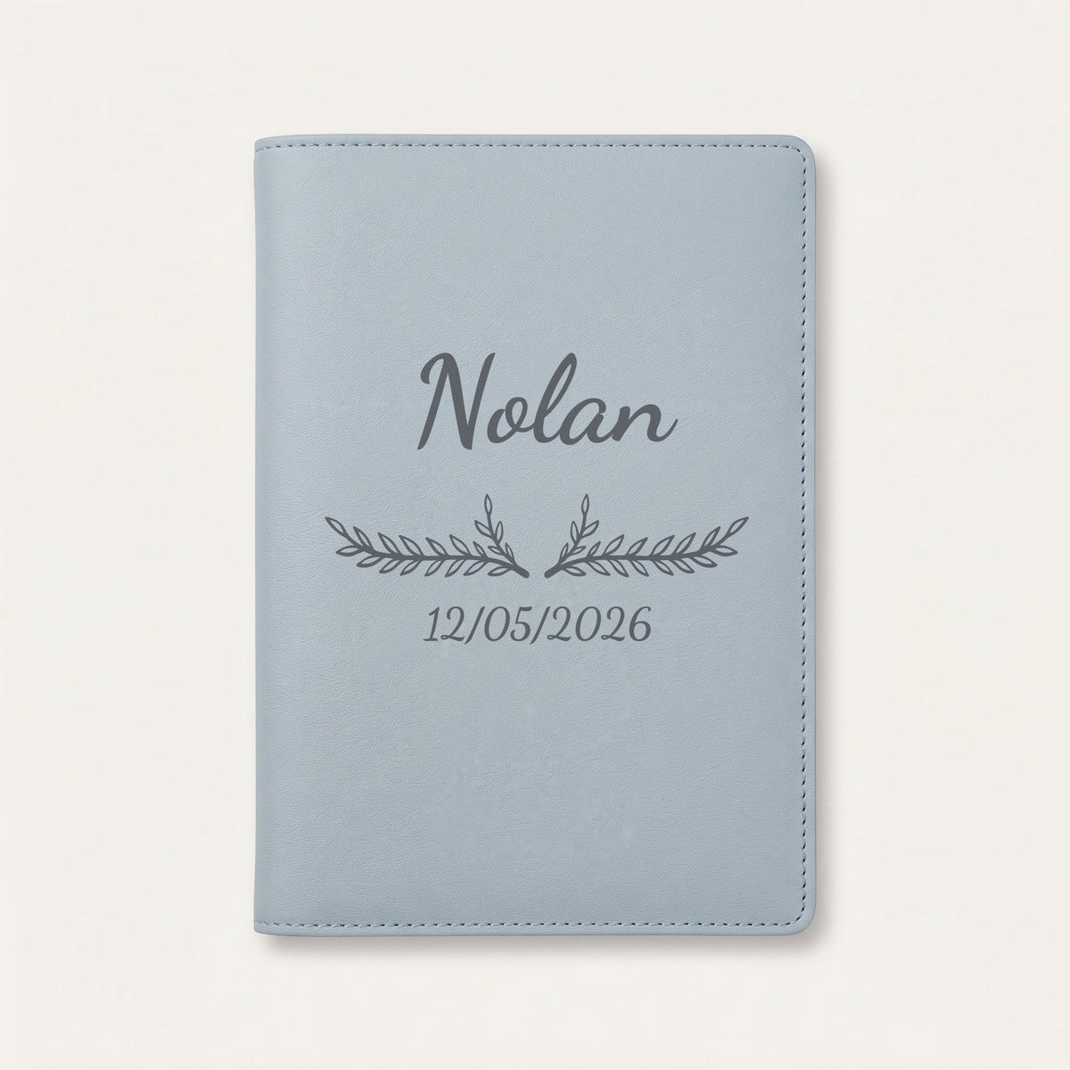 Protège carnet de santé personnalisé Nolan — Bleu nuage — prénom « Nolan », ornement Bouquet et date de naissance « 12/05/2026 » gravés