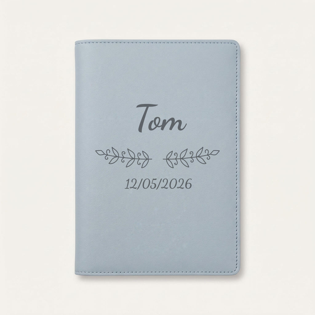 Protège carnet de santé personnalisé Tom — Bleu nuage — prénom « Tom », ornement Volutes et date de naissance « 12/05/2026 » gravés