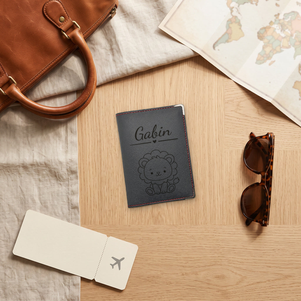 Protège-passeport bébé personnalisé – Lion — fermé, gravé « Gabin » avec le motif lion, prêt pour le départ en voyage (visuel de mise en scène, surpiqûre Rouge)